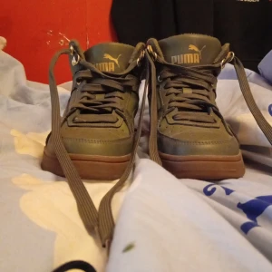 Gröna sneakers från Puma - Snygga gröna sneakers från Puma med hög design och snörning. Skorna har en robust brun sula och är perfekta för en casual look. Puma-loggan syns tydligt på sidan och tungan.