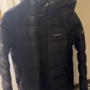 Svart dunjacka från Peak Performance - Säljer en svart dunjacka från Peak Performance. Jackan har en quiltad design och är långärmad med en dragkedja framtill. Perfekt för kyligare väder. Köpt på Intersport 