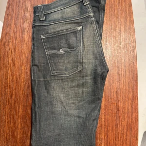 Mörkblå jeans med kontrastsömmar - Snygga jeans från märket nudie, byxorna är i storlek 30/34 och är i modellen grim tim. Riktigt fräscha byxor som är väldigt trendiga! Ända defekterna är sömmen på höger bakficka och ett litet hål under höger knä.