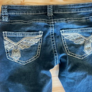 Blå bootcut jeans från Gina Tricot - Snygga blå bootcut jeans från Gina Tricot med broderade detaljer på bakfickorna. Jeansen har en klassisk femficksdesign och en bekväm passform. Perfekta för en avslappnad stil. Använda 1 gång och köptes för 399kr