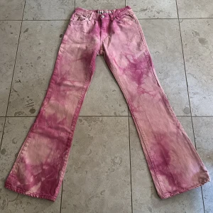 Coola vintage jeans - Unika rosa vintage jeans med en cool och avslappnad stil. Byxorna har en klassisk femficksdesign och knappgylf. Perfekta för att ge din outfit en färgglad touch. Midjemått tvärsöver: 32 cm. Innerbenslängd: 81 cm.