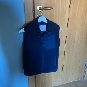 Svart fleeceväst med dragkedja - Säljer en stilren svart fleeceväst från Uniqlo. Västen har en praktisk dragkedja och en bröstficka.västen passar en person som är runt 155.hör av er vid frågor😄