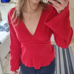Röd v-ringad topp  - Snygg röd slutsåld v-ringad topp från Gina Tricot med långa ärmar och knytband som man knyter i ryggen. Använd 1 gång. Nypris: 299 kr