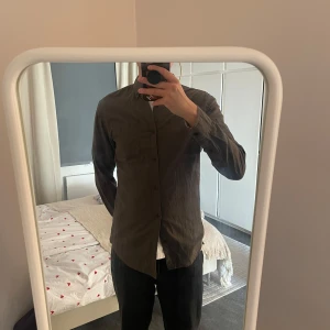 Mörk grön långärmad skjorta - Säljer en stilren grå långärmad skjorta med knappar framtill. Skjortan har en bröstficka och är perfekt för en avslappnad look. Passar bra till både jeans och chinos.