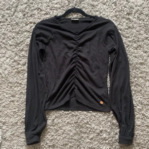 Svart ribbad tröja med knyt - Snygg svart ribbad tröja med v-ringning och knyt framtill. Perfekt för en stilren look. Långärmad design med en liten detalj vid nederkanten.💓