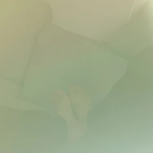 Bild på en soffa - Bilden visar en grå soffa med en person som sitter med benen uppdragna. Personen har svarta byxor på sig.