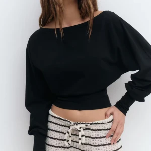 Svart croppad långärmad tröja - Svart croppad tröja med bred resår i midjan och långa ärmar. Tröjan har en avslappnad passform med lite lösare ärmar och en bred, något båtformad halsringning som ger en snygg offshoulder-look. Perfekt till jeans eller kjol för en trendig stil. Helt ny med prislapp kvar.