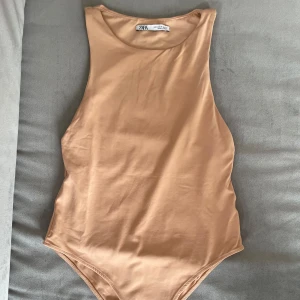 Beige ärmlös body från Zara - Snygg beige body från Zara med högt skurna ärmhål och rund halsringning. Modellen är ärmlös och har en clean, minimalistisk look som passar perfekt till jeans eller kjol. Mjuk och stretchig i materialet för en bekväm passform.
