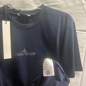 Mörkblå Stone Island t-shirt i bomull - Snygg mörkblå t-shirt från Stone Island med klassisk logga tryckt på bröstet. T-shirten har rund halsringning och korta ärmar. Tillverkad i mjuk bomull som känns skön mot huden. Perfekt för en clean och stilren look.