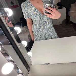 Blommig kortklänning med v-ringning - Söt blommig klänning med v-ringning och korta ärmar. Klänningen har blå och gula blommor på vit botten och en lätt utställd kjol. Perfekt för sommarens alla tillfällen! Nytt skick 💗💗