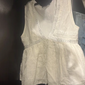 Vit broderad blus från Zara - Supersöt vit blus från Zara med djup v-ringning och broderade detaljer. Blusen är ärmlös och har spetsinslag längs ringningen och midjan. Den har en lätt volang nedtill och är gjord i ett tunt, luftigt bomullstyg. Perfekt för en fräsch och romantisk look.❤️storlek M men passar mindre 