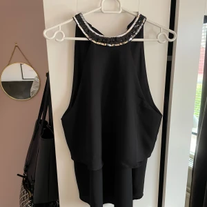 Svart paljettprydd halterneck topp från ONLY - Säljer en svart halterneck topp från ONLY med glittriga paljetter längs kragen och en stor rosett i nacken som man knyter. Toppen är ärmlös och har en elegant, lös passform. Toppen är aldrig använd 😊