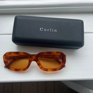 Casena solglasögon från Corlin  - Snygga solglasögon från Corlin med rektangulära bågar i brunmelerad färg och bruna glas. Nästintill oanvända.