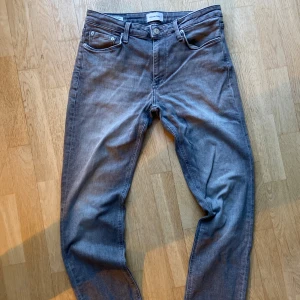 Grå jeansbyxor från Jack and Jones - Säljer ett par grå jeansbyxor från Jack and Jones med klassisk femficksdesign och raka ben. Byxorna har normal passform och är tillverkade i mjukt denimtyg. Perfekta för en stilren vardagslook.