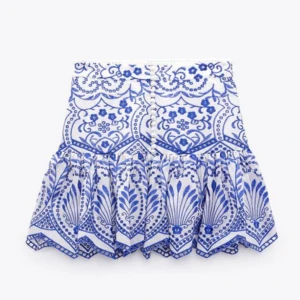 Vit och blå kortkjol från Zara - Säljer denna populära, superfina kortkjol från Zara i vitt och blått med broderat mönster och dekorativa knappar framtill. Kjolen har volangkant och är gjord i ett lätt linnematerial, perfekt för varma dagar. Snygg att styla med en enkel topp för en fräsch look. Köpte den förra sommaren och sparsamt använd 