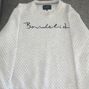 Vit tröja från Bondelid med strukturmönster - Säljer en vit långärmad tröja från Bondelid i storlek M. Tröjan har ett diskret strukturmönster och Bondelid-logga broderad framtill. Rund halsringning och mjukt material som passar perfekt till vardags.
