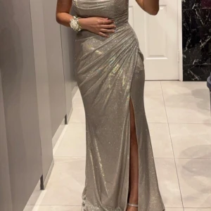 Glittrig långklänning från Dressroom - Säljer en elegant glittrig långklänning från Dressroom i en vacker champagne färg. Klänningen har en draperad design med breda axelband och en smickrande passform. Perfekt för speciella tillfällen!                                                           Festklänning 36/38 storlek   Använd endast en gång i 7 timmar   Från Dressroom ord pris 3990kr 