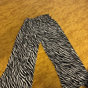 Zebramönstrade wide byxor - Säljer ett par svarta och vita byxor med zebramönster och breda ben. Byxorna har resår i midjan för extra komfort och är tillverkade i ett mjukt, lätt material. Perfekta för dig som vill sticka ut med en cool och trendig look.