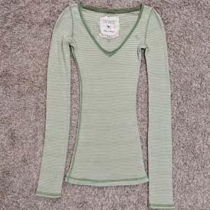 Grönrandig v-ringad tröja Abercrombie & Fitch - Slimmad långärmad tröja från Abercrombie & Fitch i ljusgrönt och vitt randigt mönster. V-ringad hals och mjukt bomullsmaterial, perfekt för lager-på-lager. Snygga gröna sömmar som detalj. Storlek M men passar mig som brukar ha S🩷(lånade bilder)