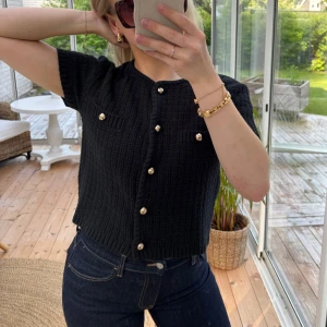 Svart kortärmad kofta med guldknappar - Säljer en superfin svart stickad kofta med guldknappar från H&M!🖤 (ena knappen sitter lite löst men kan lätt fixas). Storlek S!