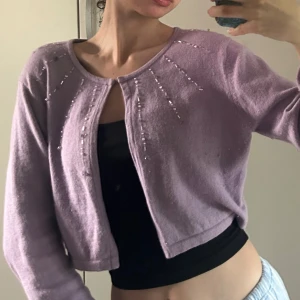 LÄGG PRISFÖRSLAG!!! Ljuslila croppad kofta med pärldetaljer - LÄGG PRISFÖRSLAG!!! Strl M, men jag är XS och den passar mig perfekt! Andra bilden är ej min! Säljer en ljuslila croppad kofta med pärldetaljer längs axlarna. Koftan har rund halsringning och långa ärmar. Perfekt att slänga över en topp för en söt look.