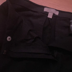 Svarta kostymbyxor från H&M - Svarta kostymbyxor från H&M med klassisk passform. Byxorna har dragkedja och knapp framtill samt raka ben. Perfekta för en stilren look.