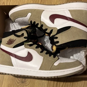 Nike Air Jordan 1 Zoom Air CMFT Olive - Säljer ett par Nike Air Jordan 1 Zoom Air CMFT i olivgrönt, vitt och vinrött. Skorna har högt skaft, svart snörning och klassisk Jordan-logga på sidan. Perfekta för dig som gillar streetwear och sneakers med unik färgkombination. Använda en gång, säljer för dom inte används, skriv om ni har några funderingar 
