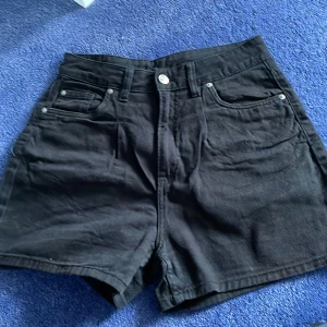 Svarta högmidjade jeansshorts H&M - Svarta högmidjade jeansshorts från H&M Divided. Klassisk femficksmodell med knapp och dragkedja framtill, bälteshällor och raka ben. Perfekta till sommaren och lätta att matcha med allt. Snygg och enkel stil som funkar till många looks.