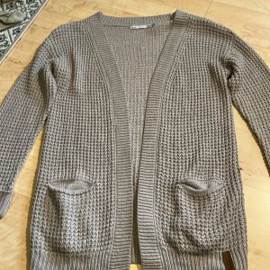 Grå stickad kofta - Det är en stickad tröja i färgen grå. Den är en lite längre kofta och har uppvikta ärmar. Det finns två fickor som inte är jättestora, men lagom stora för t.ex nycklar m.m. Även fast fickorna är helt öppna så har jag märkt att de håller sakerna kvar bra. Den är i storlek 150cm men kan bäras av längre oxå.