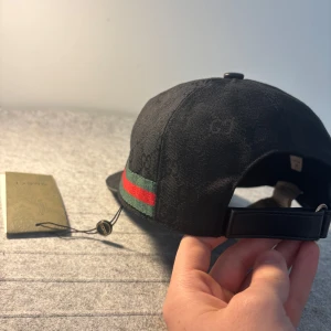 Svart gucci keps - Skriv dm för video eller prisförslag! Snygg svart keps från Gucci med diskret GG-monogram över hela kepsen och klassiska gröna och röda ränder på sidan. Justerbar rem baktill för perfekt passform. Perfekt accessoar för en trendig look. Storlek ”M”