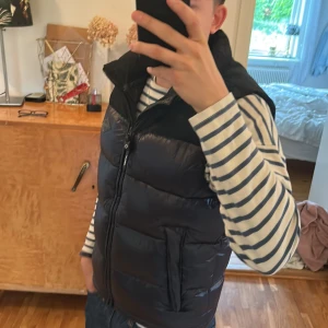 Svart dunväst från Replay - Snygg svart dunväst från Replay med hög krage och två stora fickor framtill. Västen har quiltad design och stängs med dragkedja. Perfekt för lager-på-lager och håller dig varm under kyliga dagar.