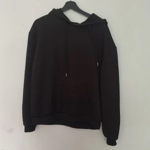 Svart hoodie med julmotiv från SHEIN - Svart hoodie från SHEIN med tryck av skelett i tomteluva och julmotiv på ryggen. Tröjan har huva med dragsko och en stor ficka framtill. Tillverkad i mjuk polyesterblandning med lite stretch.