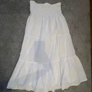 Vit långkjol med broderade detaljer - Superfin vit långkjol med broderade blommor och smock i midjan. Kjolen har volanger och är gjord i luftig bomull, den har inga tecken på användning 💕(som man kan se på bilderna)