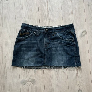 Blå lågmidjad jeanskjol  - Mörkblå fransad lågmidjad jeanskjol från Yessica i fint skick. Kan inte hitta storlek men skulle säga S/M. Tvärs över midjan är det 40 cm och den är ca 32-33 cm lång. Använd gärna köp nu!