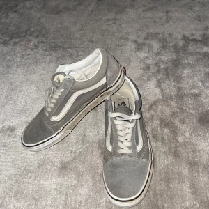 Gråa Vans Old Skool sneakers - Säljer ett par klassiska Vans Old Skool sneakers i grå mocka och vitt. Skorna har vit sula, vit sidestripe och snörning framtill. Perfekta för en avslappnad och stilren look.🙌