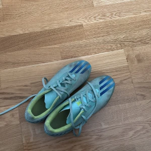 ADIDAS X SPEEDPORTAL .4 FG AL RIHLA - TURKOS/BLÅ/GULFör spel på naturgräsplaner - Säljer ett par ljusblåa Adidas fotbollsskor med blå ränder och gula detaljer. Skorna har snörning och är designade för att ge bra grepp på planen med sina dobbar. Perfekta för dig som vill sticka ut på fotbollsplanen.