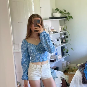 Blå blommig croppad sommarblus -  blå croppad blus från newyorker med vitt blommönster. Toppen har långa puffärmar, v-ringning och knappar framtill. Perfekt för sommaren men lite liten för mig tyvärr…
