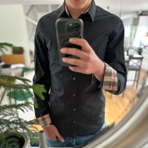 Svart burberry skjorta - Säljer en svart skjorta från Burberry. Perfekt för dig som gillar stilrena plagg med lyxig känsla. Den är använd ett fåtal gånger skick 9/10. Priset är ej huggit i sten 🪨(nypris ca 3999) Skriv om ni har några funderingar