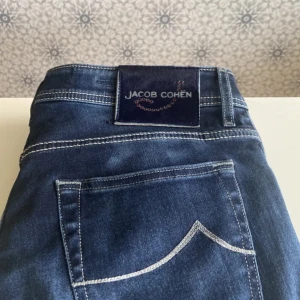 Jacob Cohen jeans  - Snygga blå jeans från Jacob Cohen med klassisk femficksdesign och kontrastsömmar. Jeansen har normal passform och raka ben, perfekt för en stilren look. Märkespatch baktill i midjan.