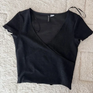 Svart glittrig fest topp  - Snygg svart glittrig fest topp med korta ärmar och djup v-ringning. 