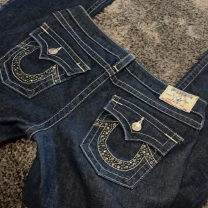 True Religion Bootcut jeans - Snygga och trendiga True Religion bootcut jeans med dekorerade bakfickor. Aldrig använda i jättebra skick. Passar mig som är 169cm, passar dock om man är kortare eller längre. Uppskattar det till en M, fråga om mått