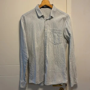 Randig skjorta från Tiger of Sweden - Snygg och stilren randig skjorta från Tiger of Sweden i ljusblått och vitt. Skjortan har en klassisk krage och en bröstficka. Perfekt för en elegant look.