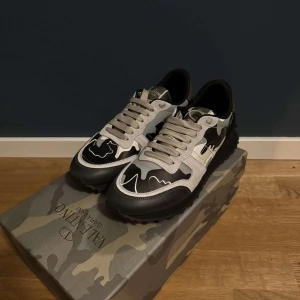 Valentino rockrunners i svart och grå - Snygga Valentino Rockrunner sneakers med ett coolt camouflage-mönster i svart och grått. Skorna har snörning och är tillverkade i en kombination av skinn och syntetmaterial. Perfekta för att ge din outfit en trendig touch. Pris kan diskuteras💫