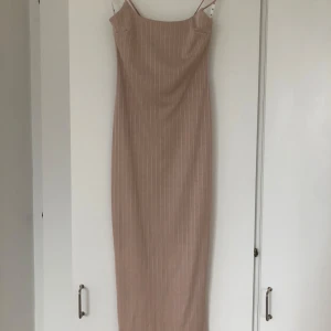 Beige axelbandslös klänning från Missguided - Snygg beige axelbandslös klänning från Missguided i samarbete med Sarah Ashcroft. Klänningen har en elegant lång design med diskreta ränder och dragkedja i ryggen. Perfekt för en stilren look.