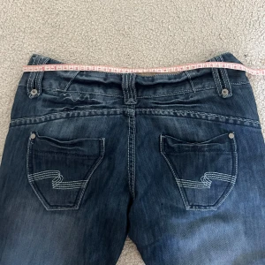Mörkblå jeans med bootcut - Snygga mörkblå jeans med bootcut-stil och coola bakfickor med dekorativa sömmar. Perfekta för en avslappnad look. De har en klassisk femficksdesign och knappgylf.