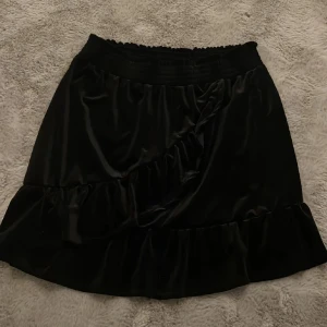 Svart kjol från Monki - Snygg svart kjol från Monki med volangdetaljer. Perfekt för att ge en elegant touch till din outfit. Den har en elastisk midja för extra komfort.
