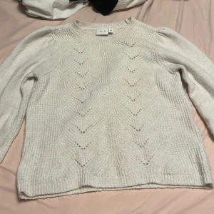 Vit stickad tröja från Vila - Säljer en vit stickad tröja från Vila med ett subtilt mönster framtill. Tröjan har långa ärmar och ribbade muddar vid ärmslut och nederkant. Perfekt för kyliga dagar!