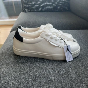 Vita sneakers från Anna Field - Snygga vita sneakers från Anna Field med svart detalj vid hälen. Skorna har klassisk snörning och en stilren design som passar perfekt till vardags. De är tillverkade i syntetmaterial och har en bekväm passform. Lappen sitter kvar och aldrig använda! Priset kan diskuteras❤️