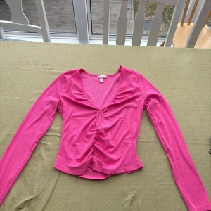 Rosa ribbad topp - Snygg rosa ribbad topp med långärmad design och v-ringning. Toppen har en fin rynkad detalj framtill som ger en extra touch. Perfekt för att liva upp garderoben! Även bra om man har någon studentfest med neontema till exempel💕💕aldrig använd.