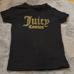 Svart t-shirt från Juicy Couture - Säljer en svart t-shirt från Juicy Couture med ett stort, gult tryck på framsidan. Perfekt för en cool och avslappnad stil. Passar barn i åldern 8-9 år.